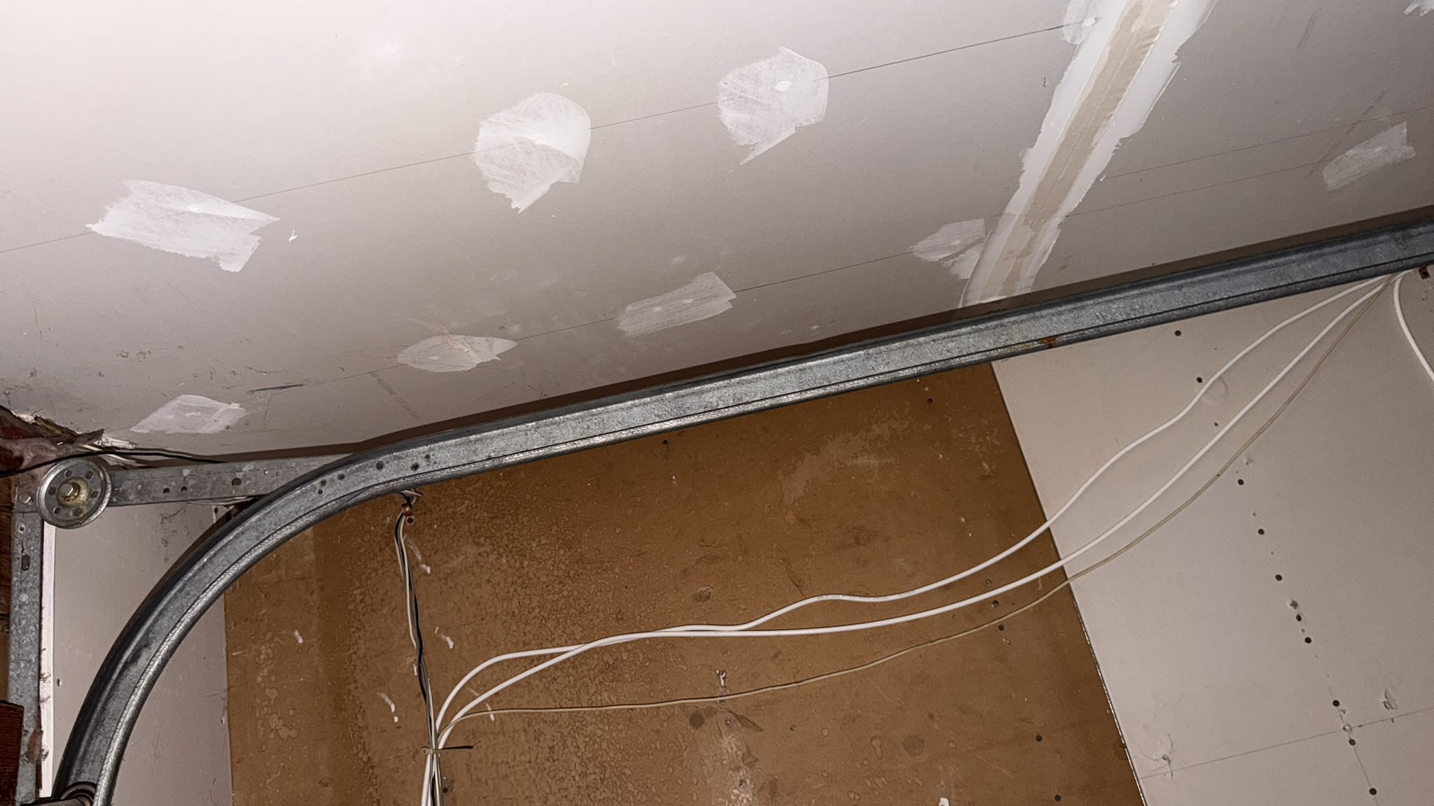 A metal garage door track running along an unfinished drywall ceiling with white patches.