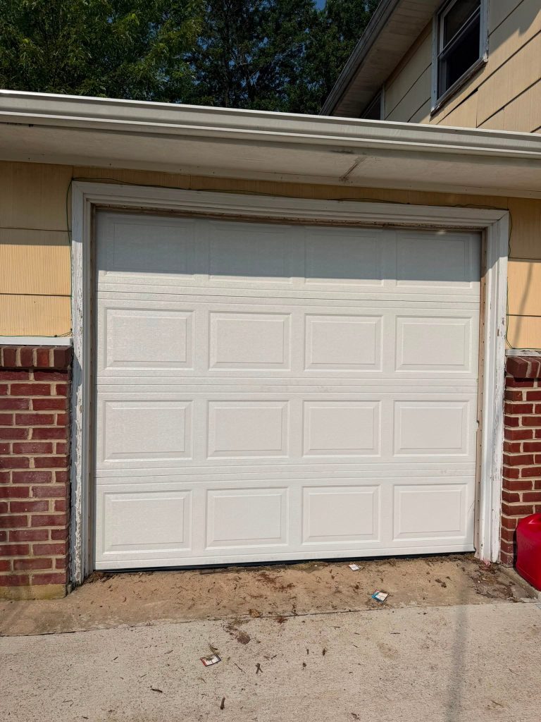 A closed white sectional garage door framed by brick and yellow siding.