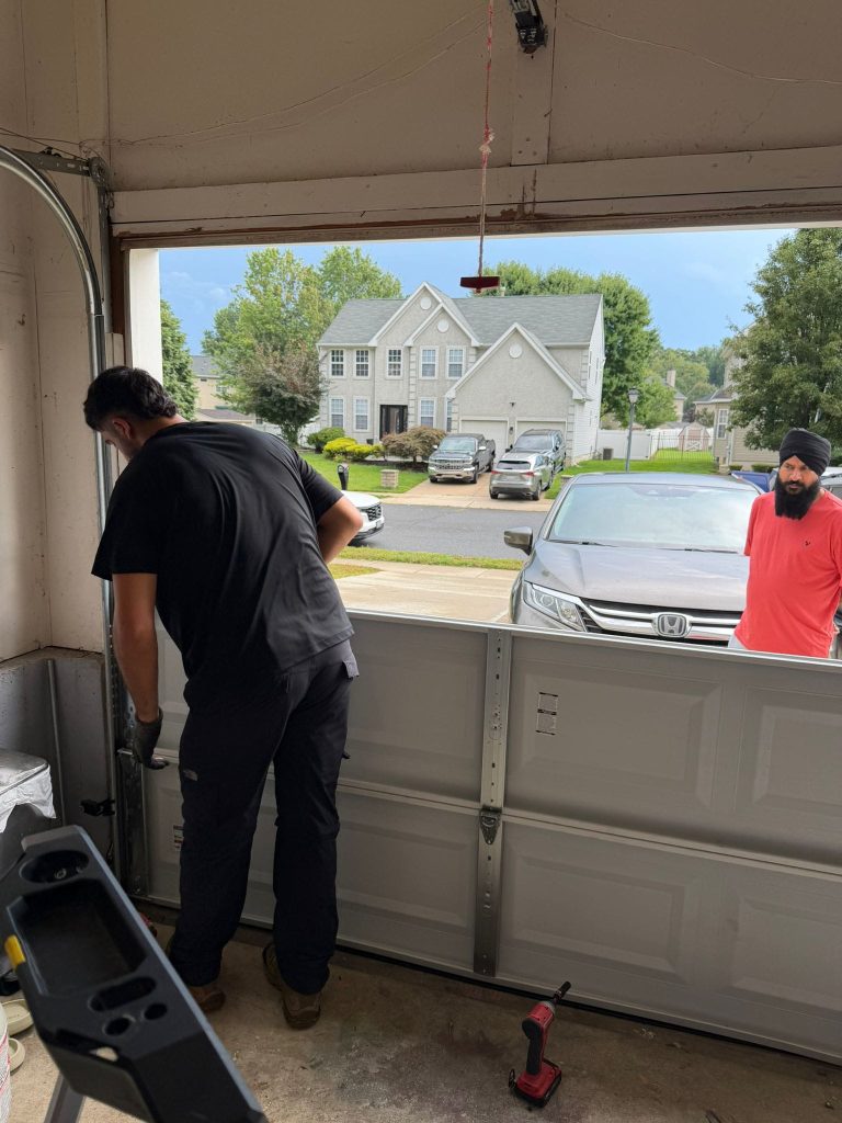 A technician is installing a garage door while another man watches from outside.