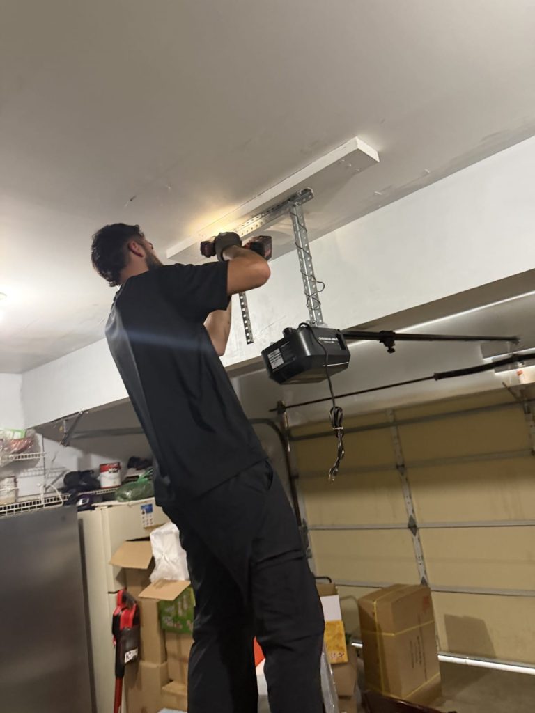 A man installing a garage door opener motor on a garage ceiling.