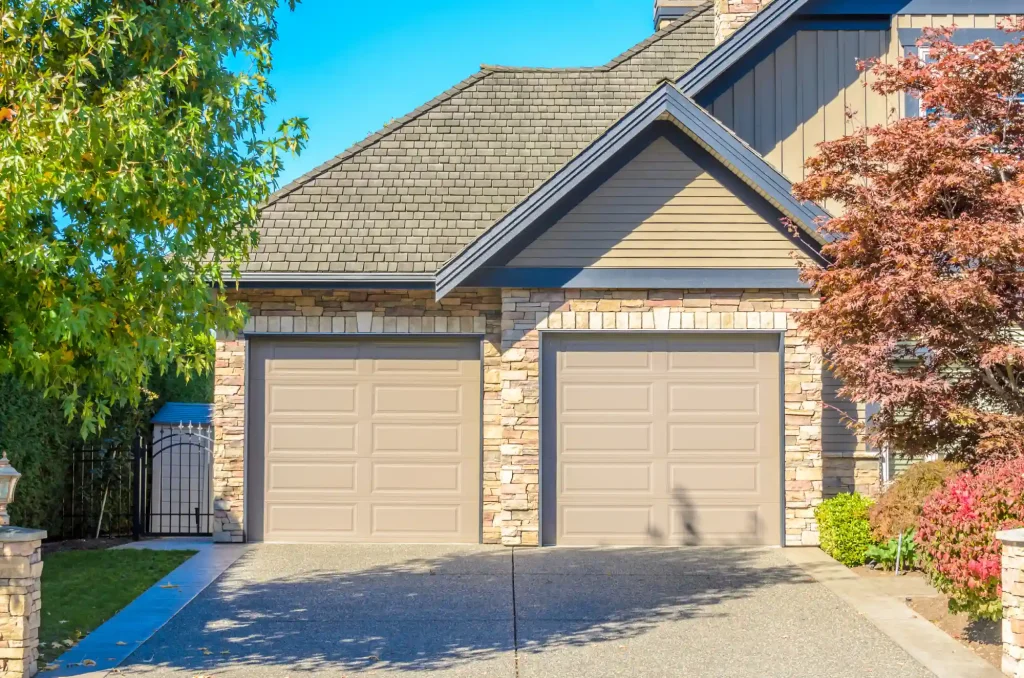 Two-car garage with beige doors and stone facade under a sunny sky.