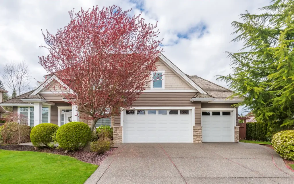 A suburban home with a paved driveway and a blossoming pink tree in the yard.