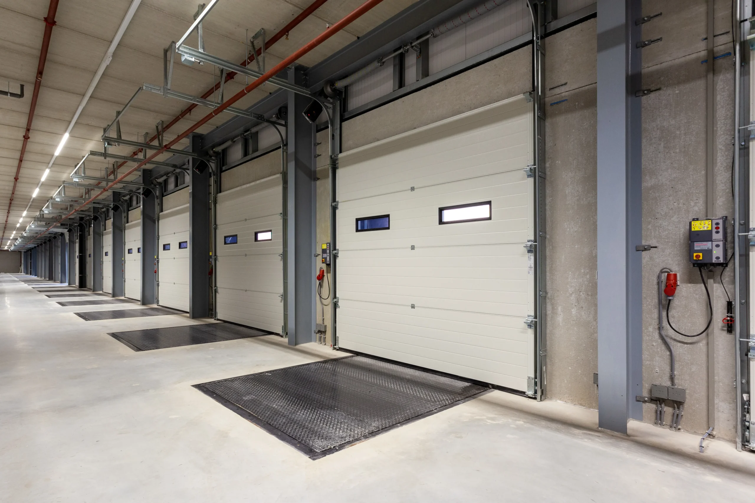 A row of closed white overhead garage doors in a spacious modern warehouse loading dock area.