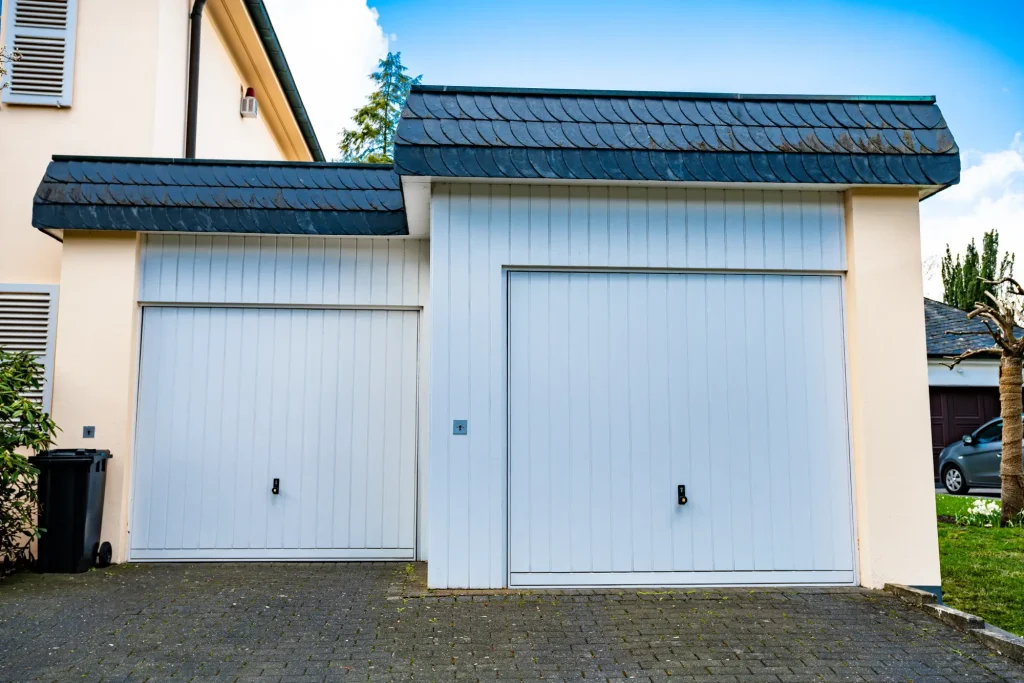 Two white garage doors with a tiled roof overhang in front of a house.